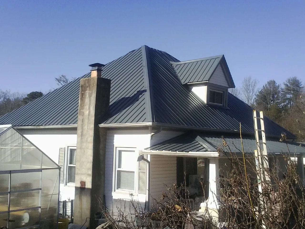 Dark blue standing seam metal roof on a white farmhouse with dormer — Slate & Tile Roof Repair by Roofing Brothers in Scottville
