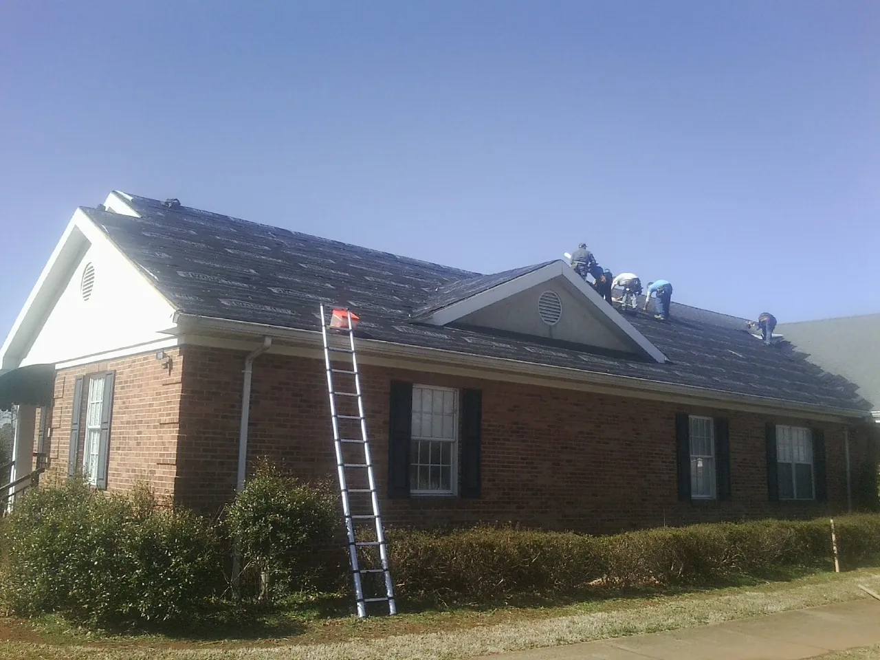 Crew tearing shingles off a brick ranch roof with a ladder set — Metal Roof Repair work by our crew in Scottville