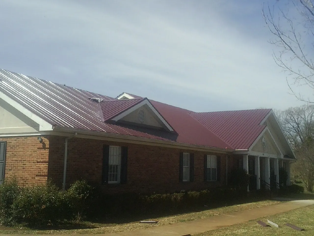Red metal roof with gabled entries on a long brick building, from a Hail Damage Roof Repair job in Scottville