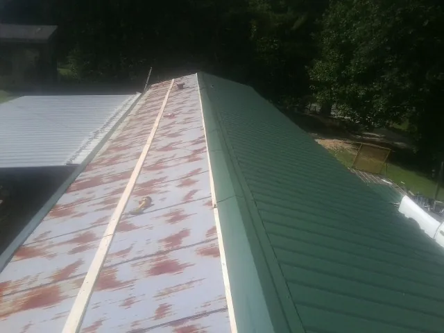 Old rusted panels beside newly installed green metal roofing — Wind Damage Roof Repair by Roofing Brothers in Scottville