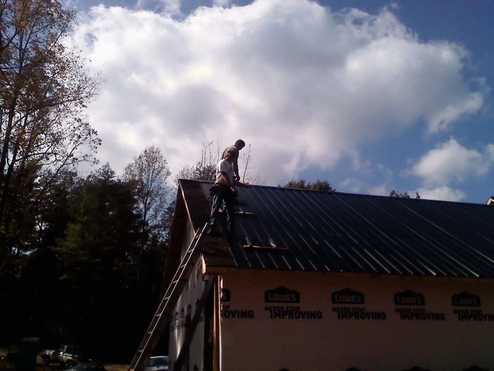 Roofer fastening dark metal panels high against a cloudy sky, from a Roof Inspection job in Scottville