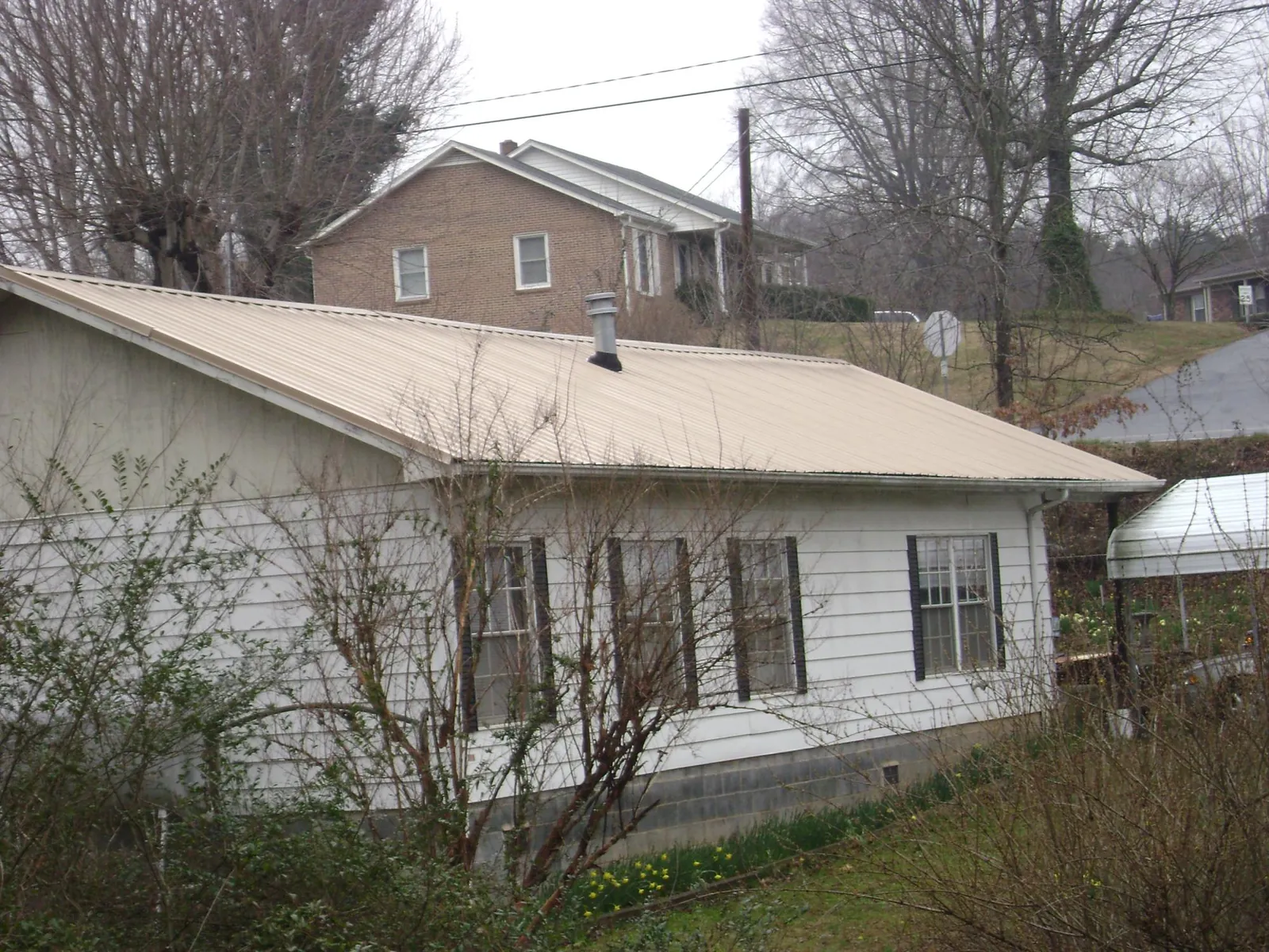 Tan metal roof on a white sided house set into a hillside — Commercial Roofing by Roofing Brothers in Scottville